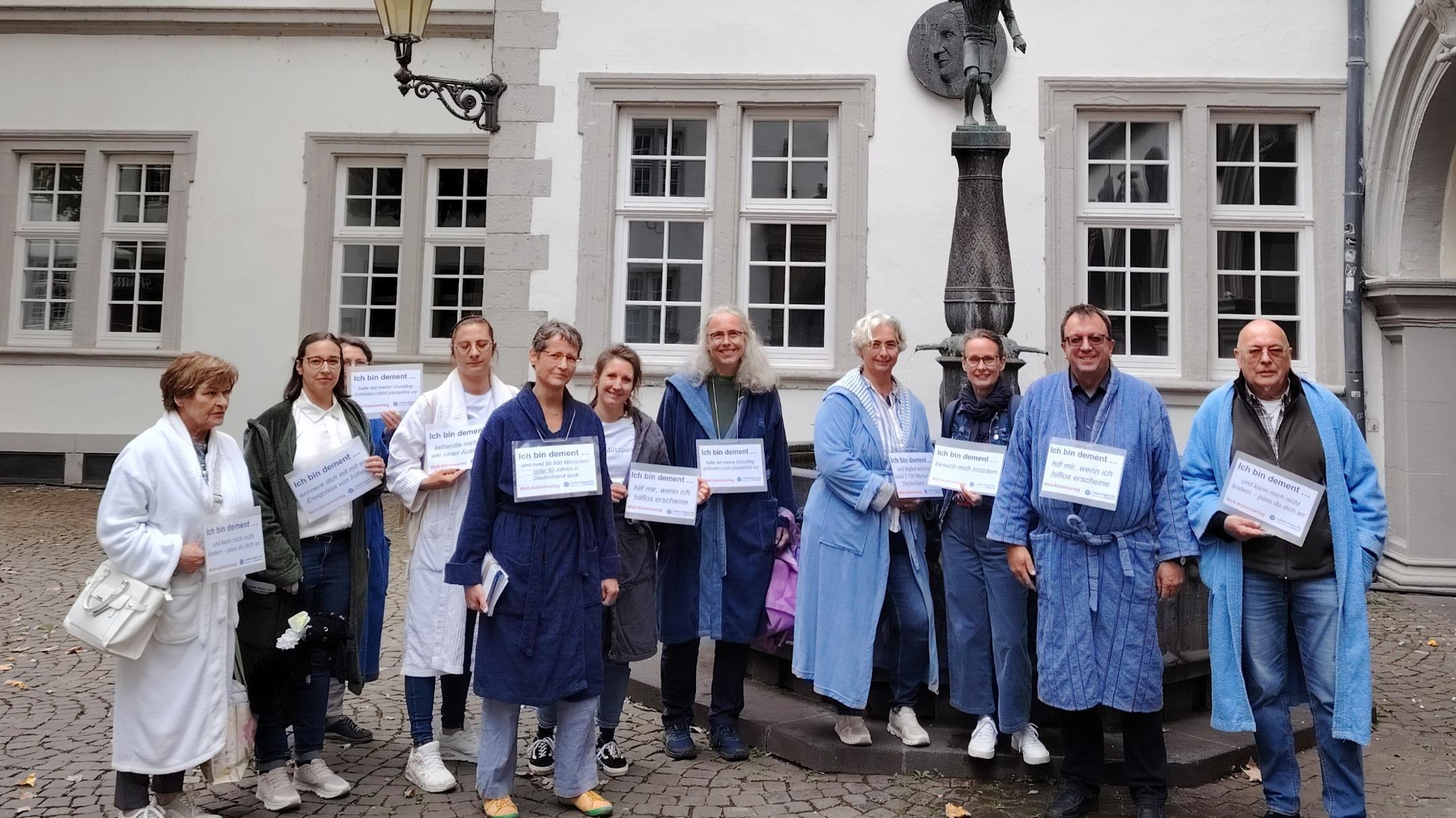 Eine Gruppe aus Personen im Bademantel in Koblenz, die mit Schildern auf Demenz aufmerksam machen